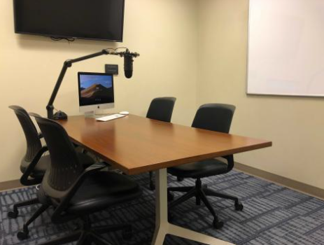 The Sound Studio in Bizzell. The space shows a table with four chairs, a Mac computer, a sound studio microphone, and a television